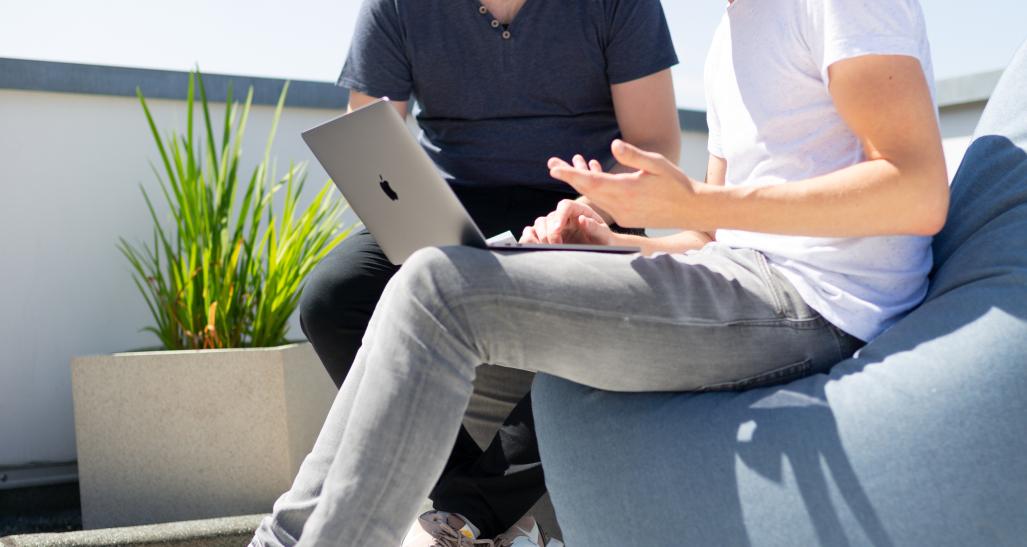 two guys sitting outside looking at a laptop together