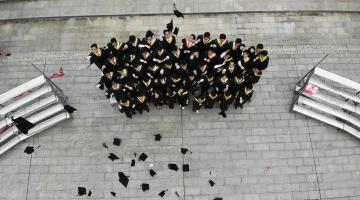 Group of kids stand outside in their cap and gowns after graduation