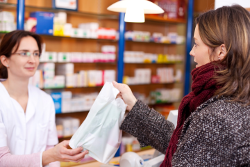 pharmacist handing a bagged prescription to a customer