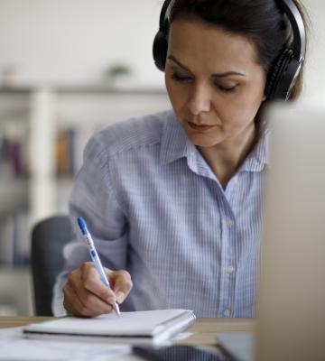 Woman wearing headphones in front of computer takes notes