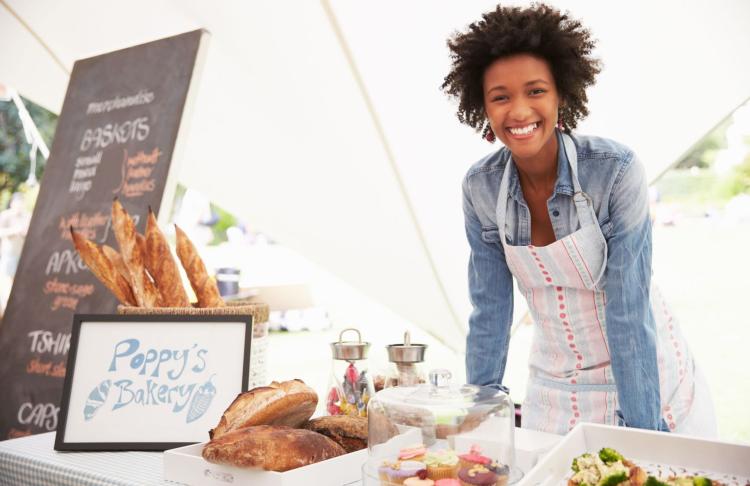 a small business owner smiles into the camera while serving at a farmers market