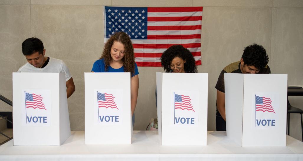 People voting standing in front of an American flag.