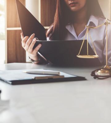 Justice scale with a woman in the background reviewing a file.