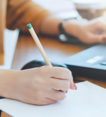 Someone taking notes next to a laptop.