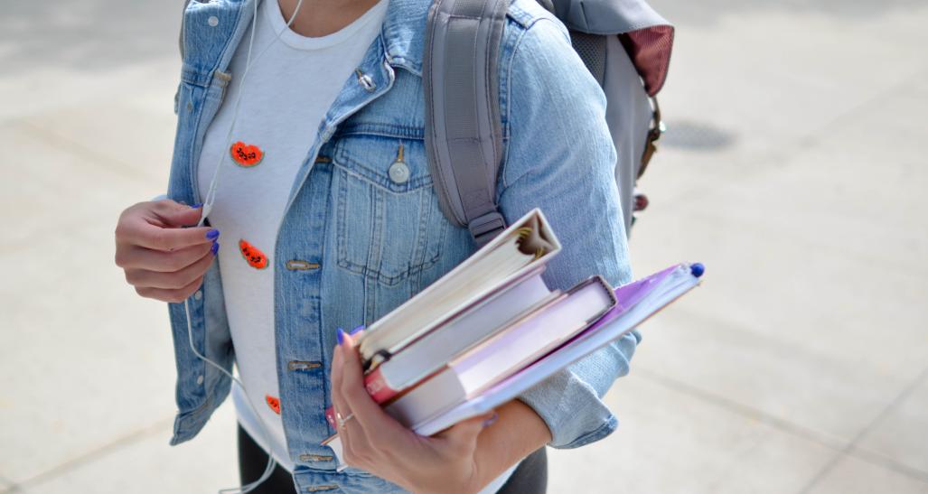 girl standing outside with a backpack and school books in her hands