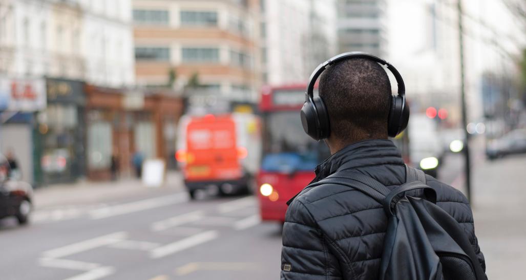 a guy stands on a busy city street with headphones on