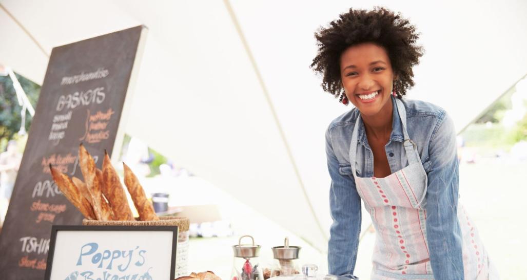 a small business owner smiles into the camera while serving at a farmers market