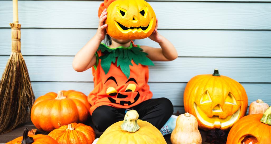 a child holds up a jack-o-lanter in front of his face for halloween