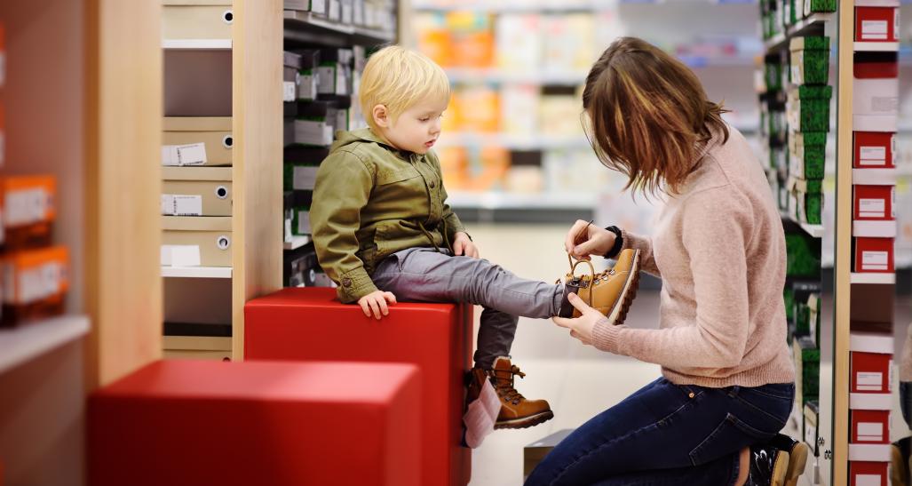 Woman helps boy try on shoes in store
