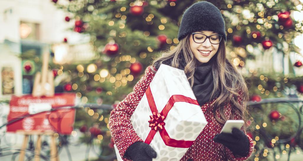 Young woman holds wrapped gift and looks at phone while holiday shopping