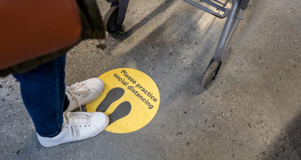 Person stands on social distancing sticker on the ground