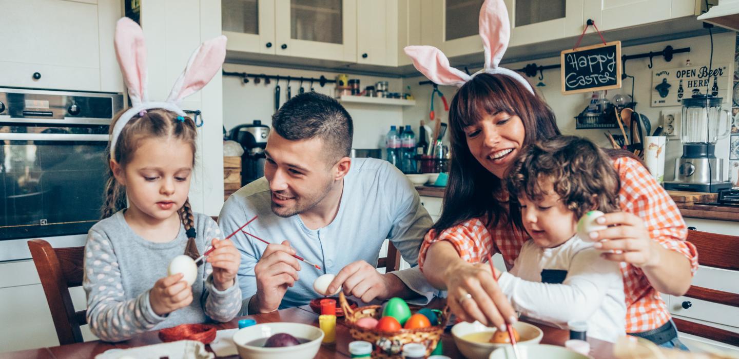 a family is painting easter eggs together at the dining table