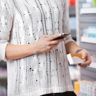a woman in a drug store shops for medicine while looking at her mobile phone