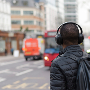 a guy stands on a busy city street with headphones on