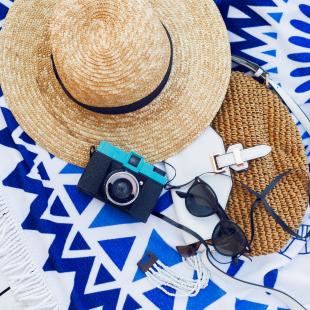 Straw hat, handbag, sunglasses and camera on a white wood background