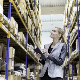 woman recording fulfillment delivery logistics in warehouse with boxes on shelves