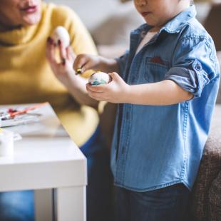 a mom and a little boy are shown painting an easter egg together in the living roome