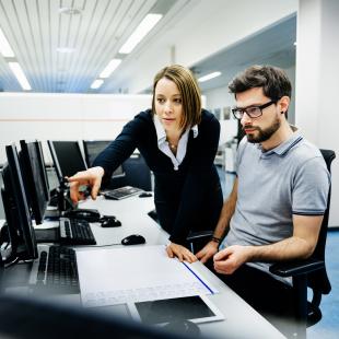 Professional woman pointing at computer for colleague