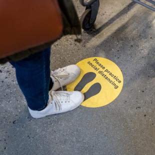 Person stands on social distancing sticker on the ground