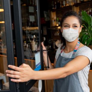 Woman opens shop doors wearing face mask