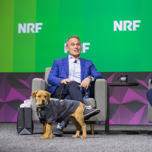 Petco CEO Ron Coughlin on the keynote stage at NRF 2023: Retail's Big Show with NRF's Matt Shay and a dog