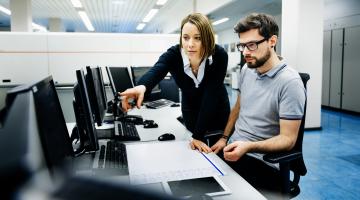 Professional woman pointing at computer for colleague