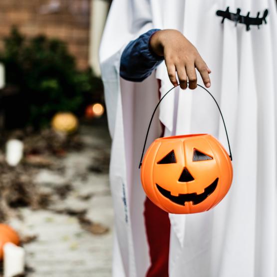 a kid in their halloween costume stands with his halloween pumpkin for trick or treating